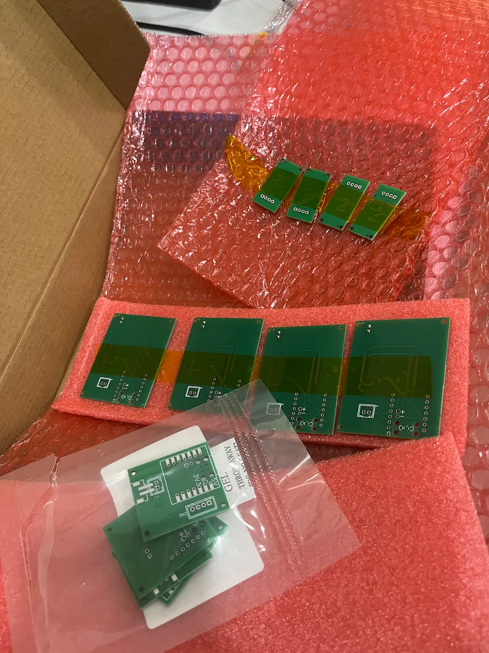 Bare custom PCBs unpacked from a JLCPCB shipping box in bubble wrap and foam
