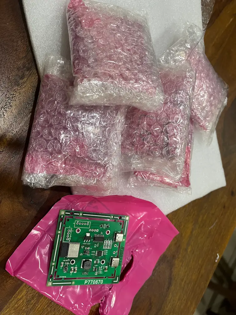 Assembled custom ESP32-C3 air quality monitor board with the rest of the batch bagged behind it